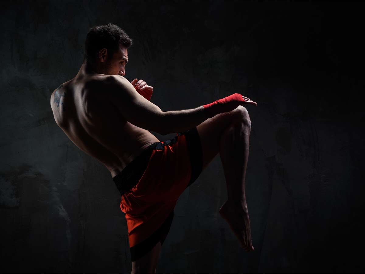 A muscular man gears up for a high, muay thai kick.