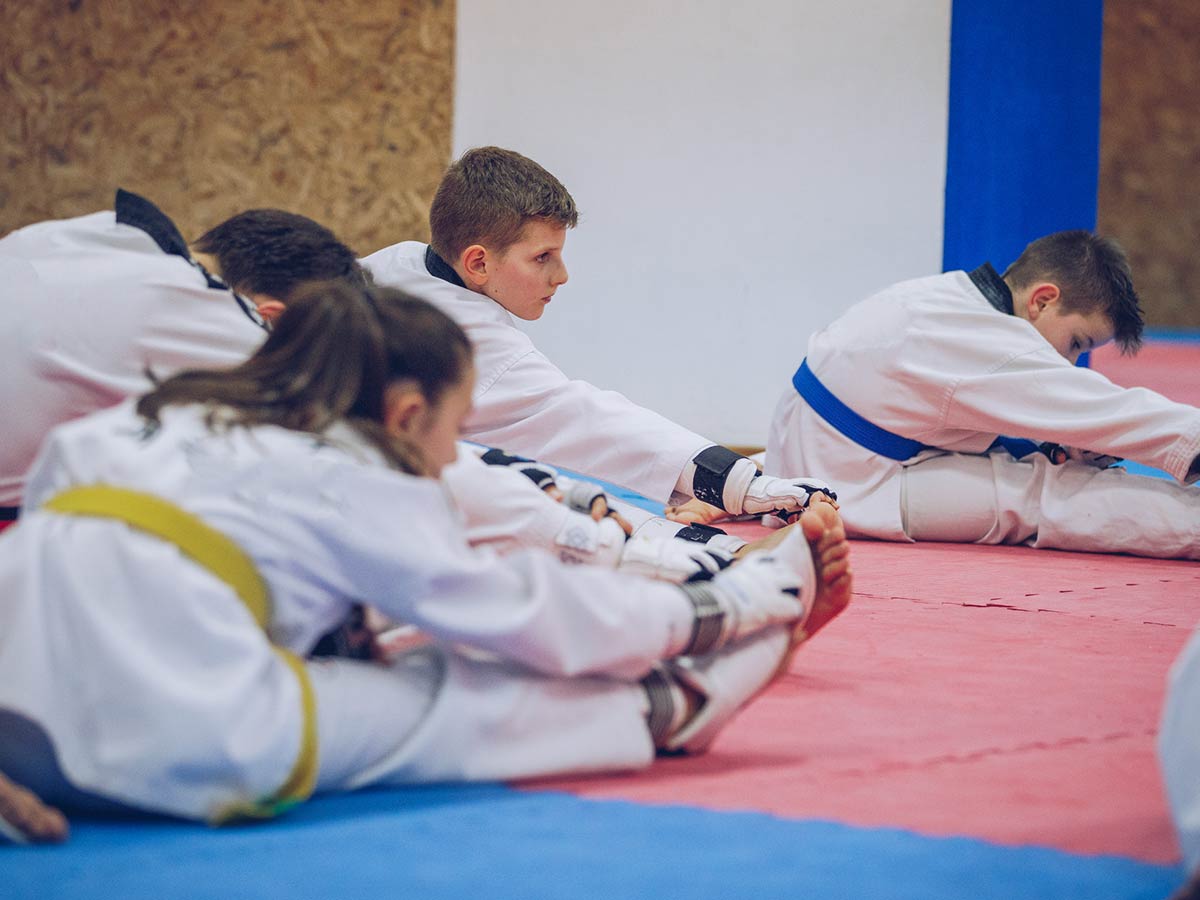 A group of young students are stretching on the ground in preparation for martial arts.